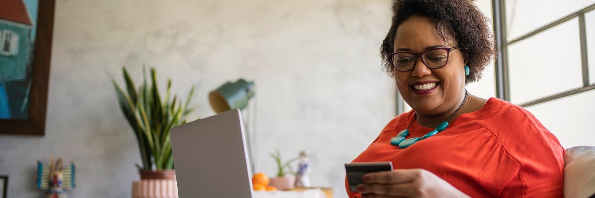 Woman smiling with laptop in lap and credit card in hand.