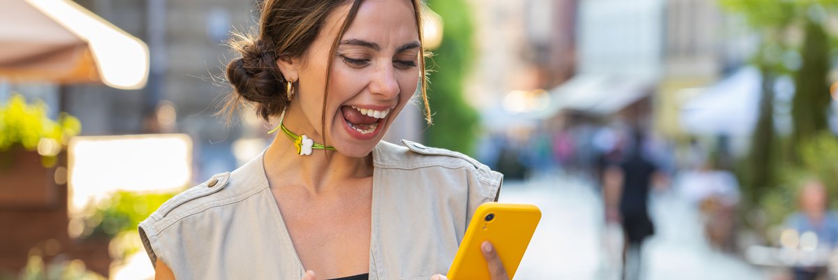 A girl celebrates something while looking at her cell phone.
