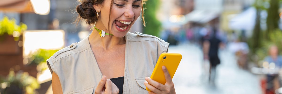 A girl celebrates something while looking at her cell phone.