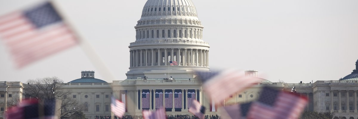 Unrecognizeable crowds waving American flags fill the Washington Mall in front of the Capitol building.