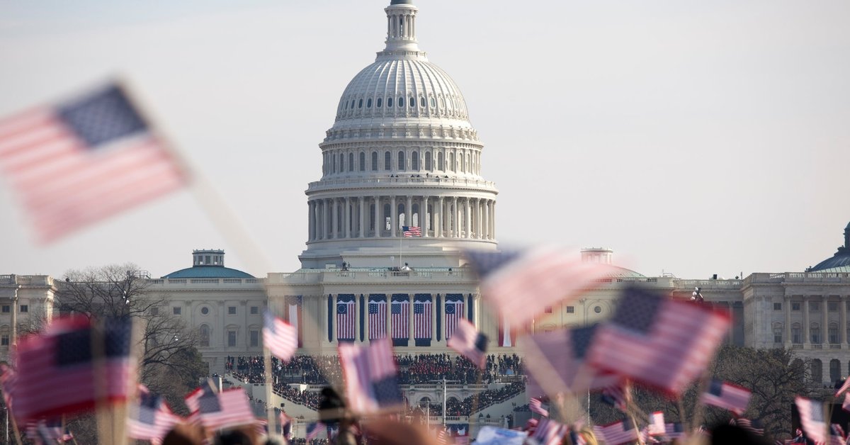 Unrecognizeable crowds waving American flags fill the Washington Mall in front of the Capitol building.