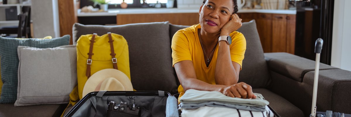 Person sitting with packed suitcases with hand to cheek in thought.
