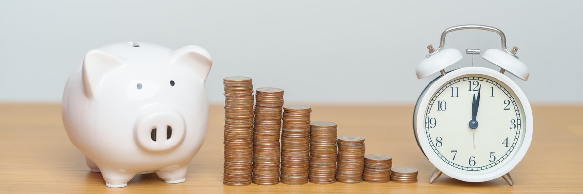 Piggy bank, stacks of coins, and an alarm clock on a table.