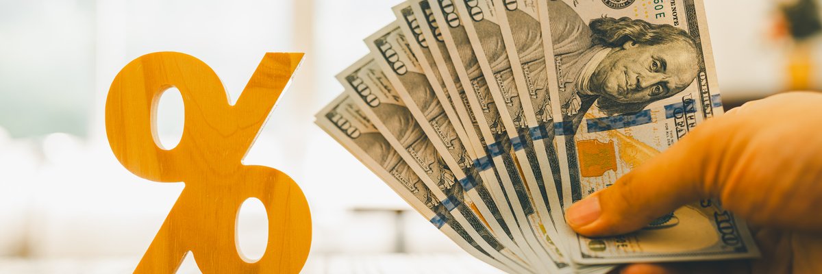 A yellow percent sign next to a hand holding a fan of hundred dollar bills.