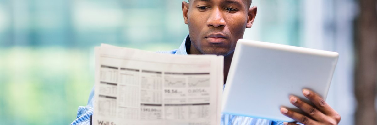 Man compares quotes from newspaper and tablet.