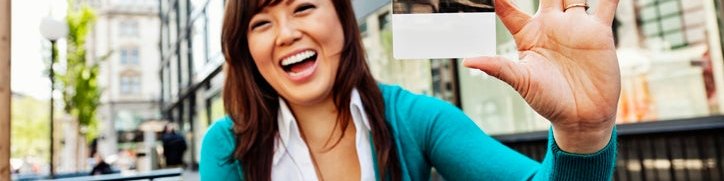 Young Asian American woman holds up a blank credit card and smiles.