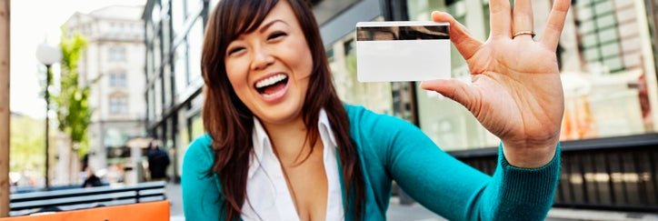 Young Asian American woman holds up a blank credit card and smiles.
