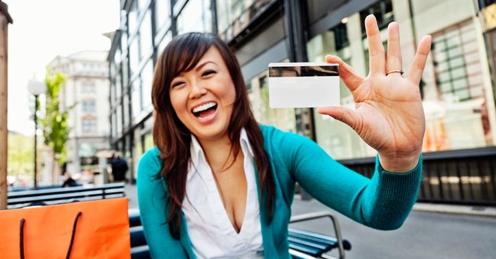 Young Asian American woman holds up a blank credit card and smiles.