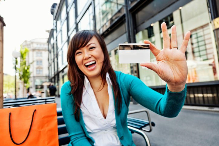 Young Asian American woman holds up a blank credit card and smiles.