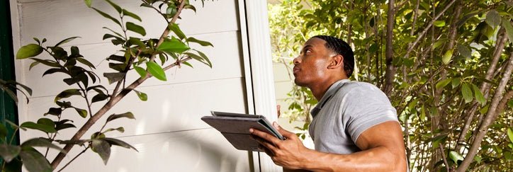 Home inspector checks the exterior walls of a house and uses a tablet to record results.
