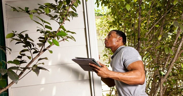 Home inspector checks the exterior walls of a house and uses a tablet to record results.