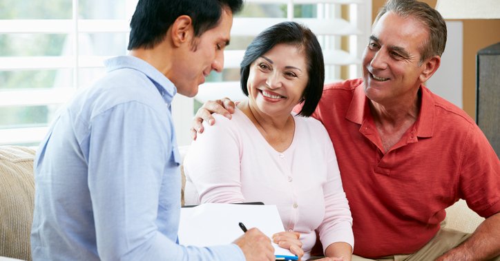Smiling couple on sofa with salesperson finalizing paperwork.
