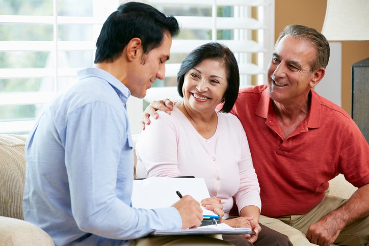 Smiling couple on sofa with salesperson finalizing paperwork.