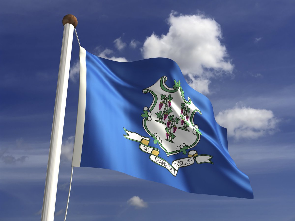 The Connecticut state flag flying in front of blue sky and white clouds.