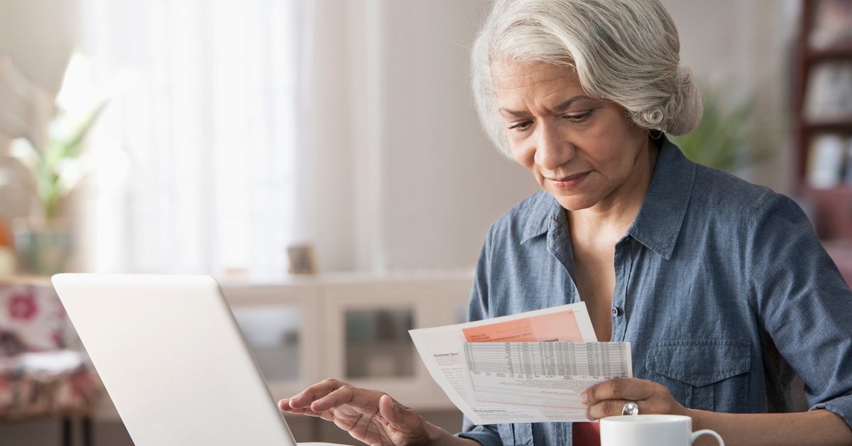 An older person pays bills using their laptop at home.