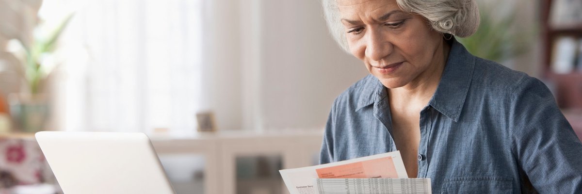 An older person pays bills using their laptop at home.