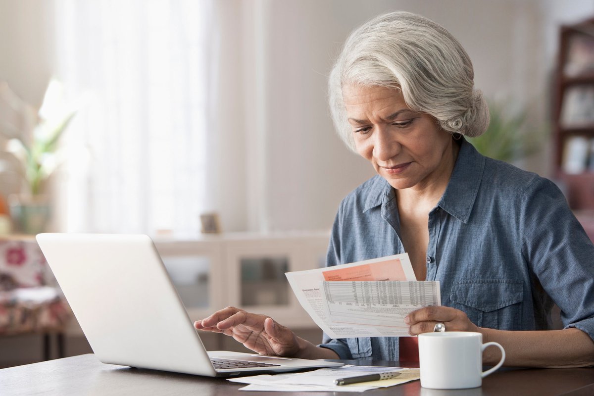 An older person pays bills using their laptop at home.