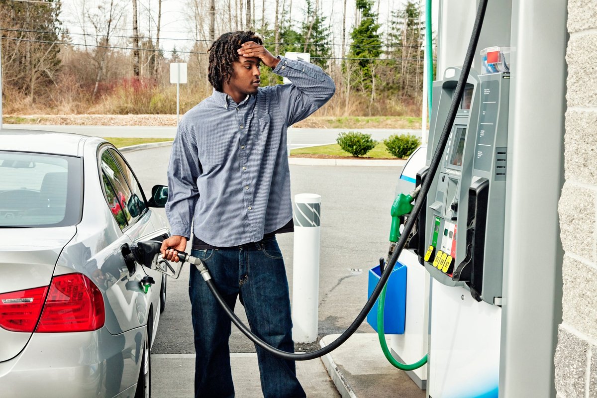A young adult pumps gasoline with a worried expression on his face.
