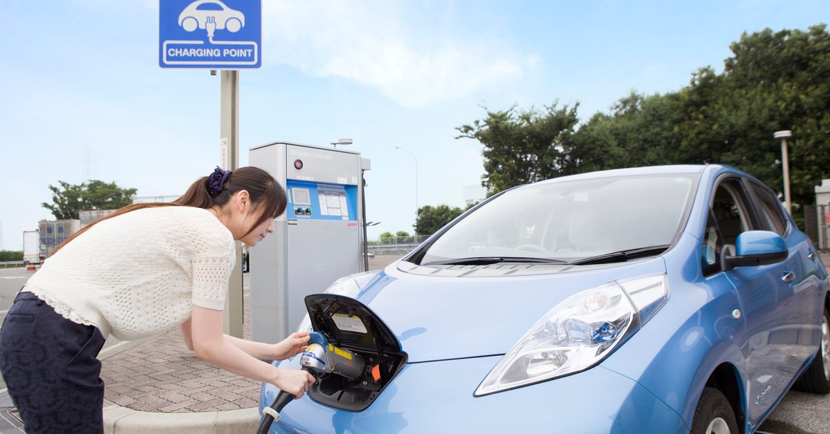 A driver charges their electric car at an outside charging port.