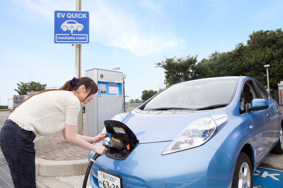 A driver charges their electric car at an outside charging port.