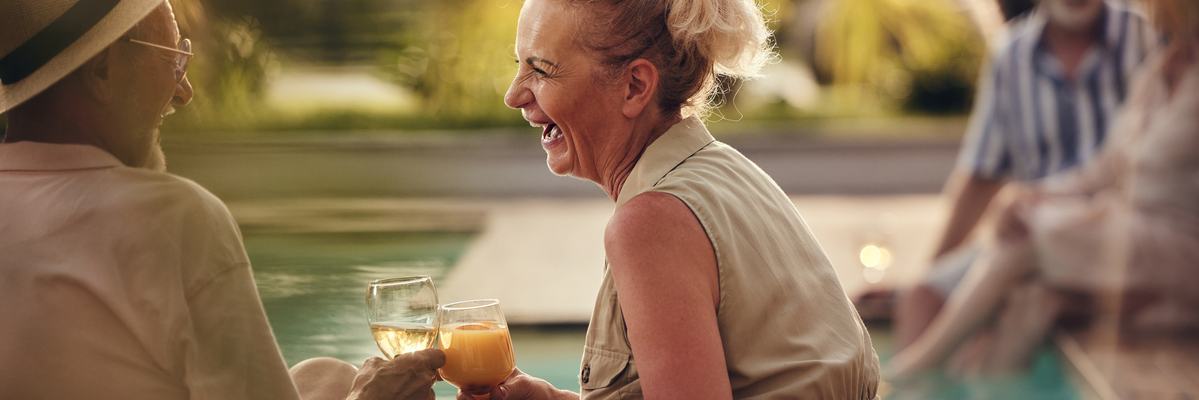 Two people clink drinks happily while sitting by a pool.
