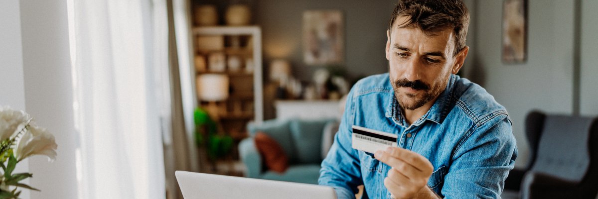 Man looks thoughtful while holding credit card and using laptop.
