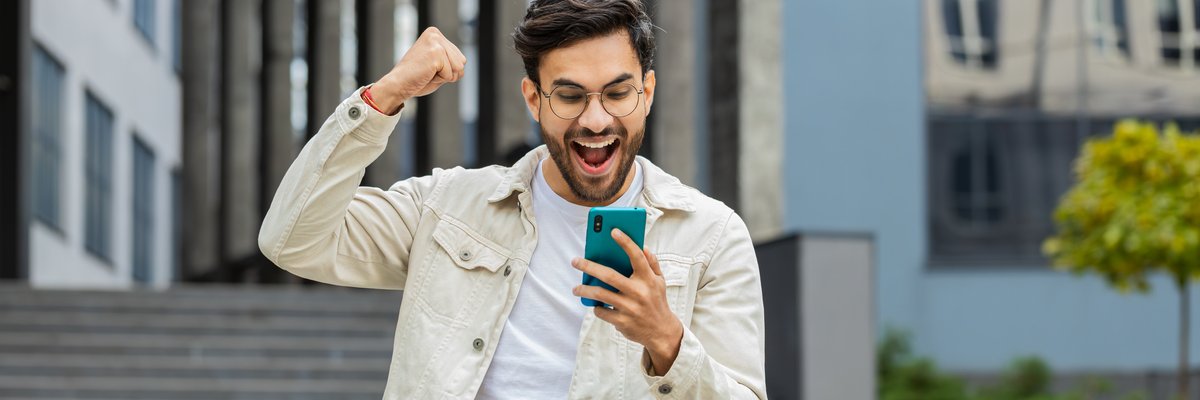 Person outdoors celebrating with fist raised while holding cellphone.