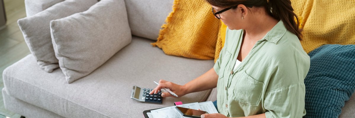 Person holding phone and paperwork on a clipboard and making calculations while sitting on a couch.