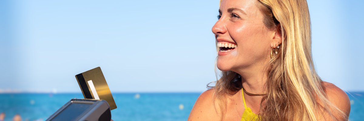 Vacationer pays for beverage with credit card at outdoor bar with beach in the background.