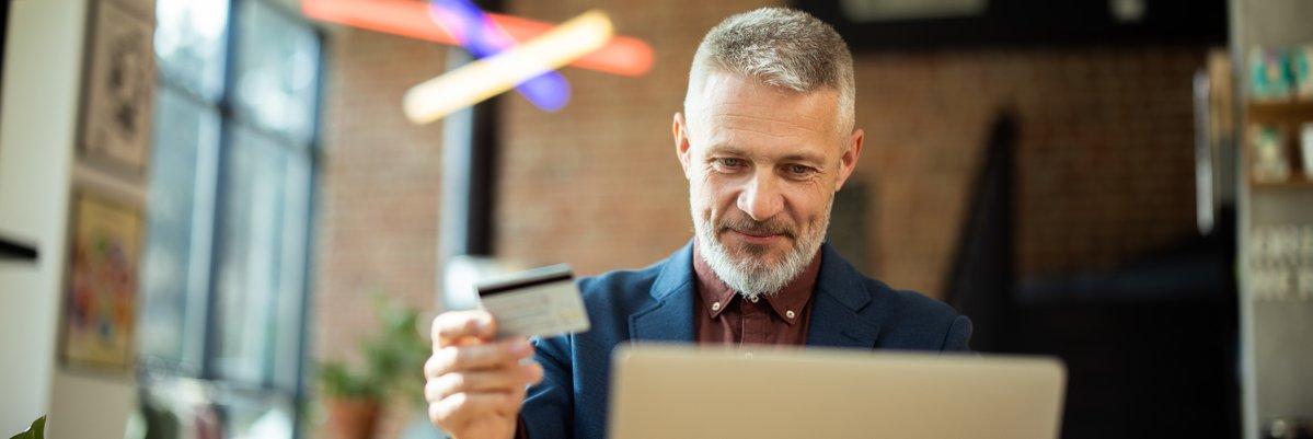 Well dressed mature man holds credit card while using laptop.