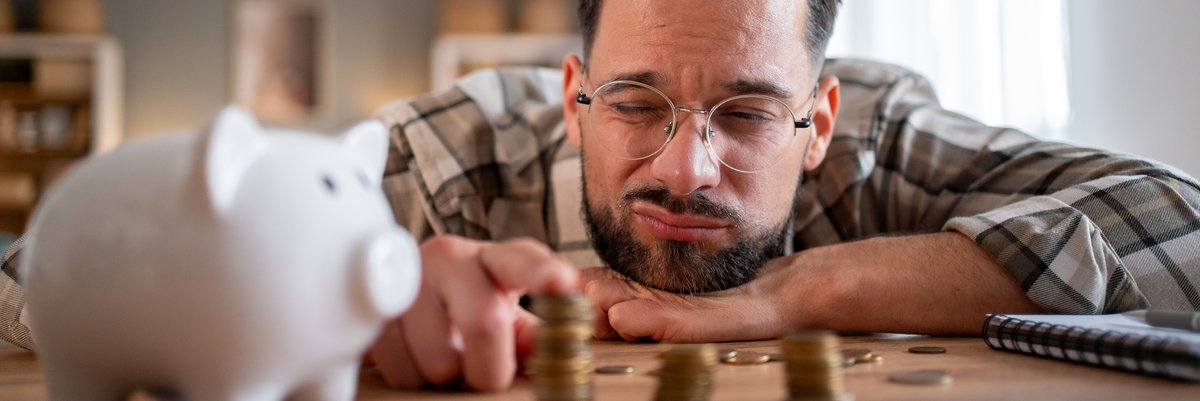 Man squinting while counting stacks of coins next to piggy bank.