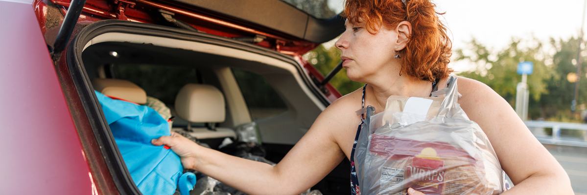 Woman unloading groceries from trunk of vehicle.