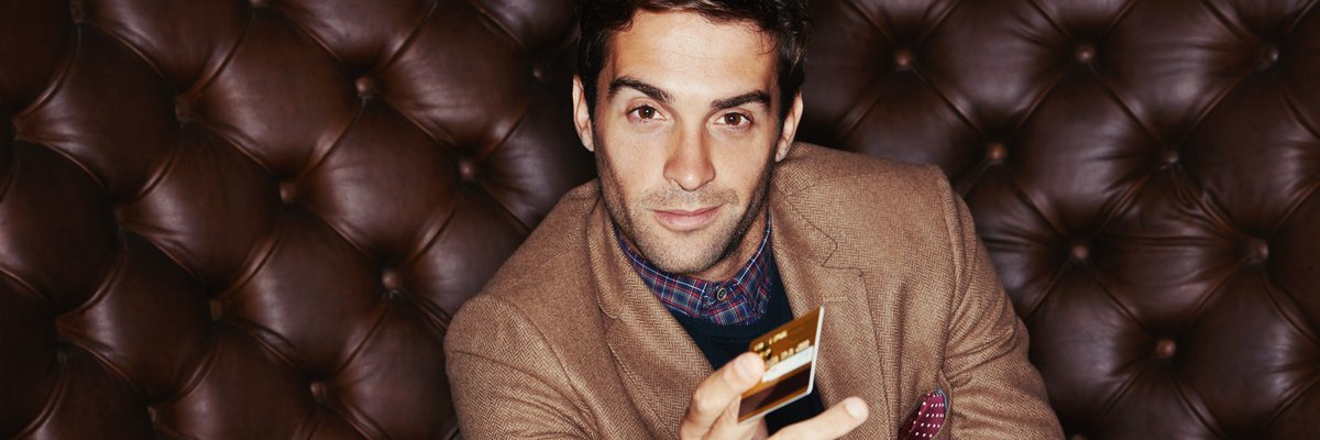 Man in suit with plush background holds a credit card with confidence.