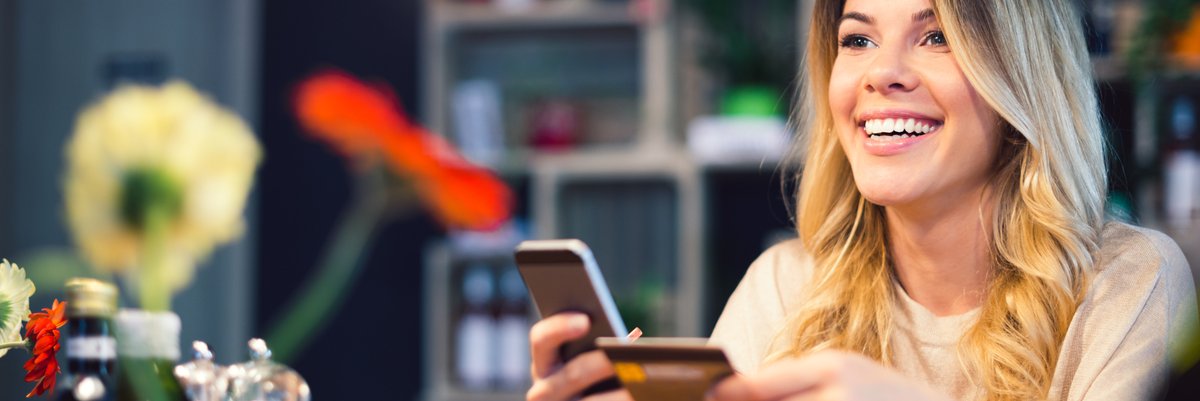 Woman smiling holding credit card and cell phone.