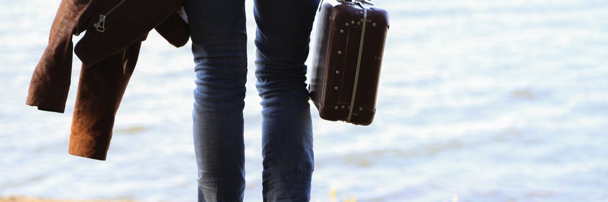 Man standing on riverbank with suitcase in tow.