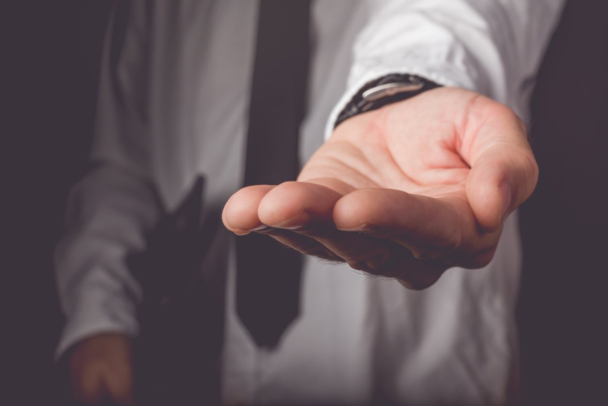 Man in shirt and tie shrouded in darkness, hand reaching out for someone to put something in it.