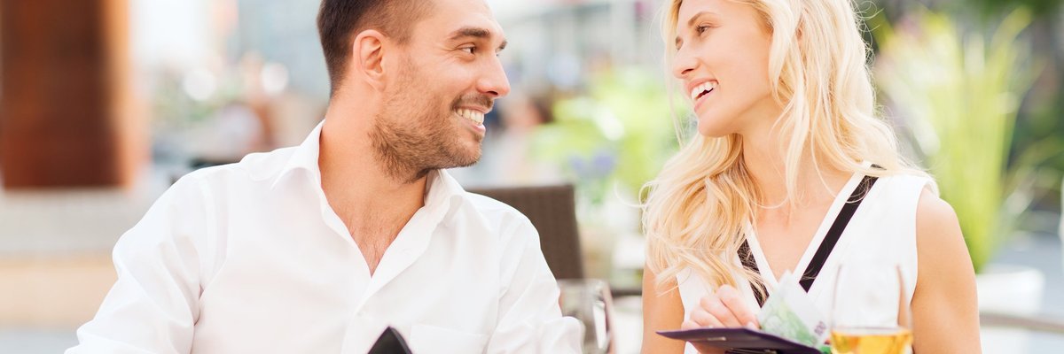 Young couple beaming at each other while taking care of the bill together at a restaurant.