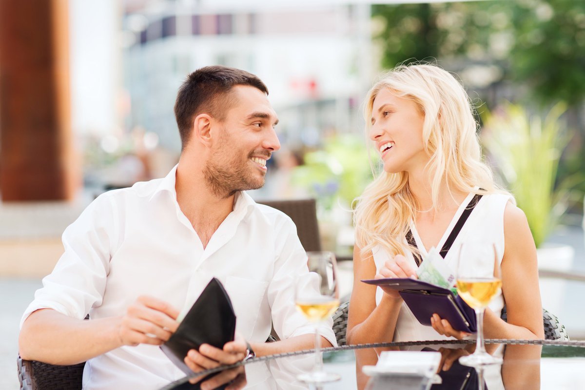 Young couple beaming at each other while taking care of the bill together at a restaurant.