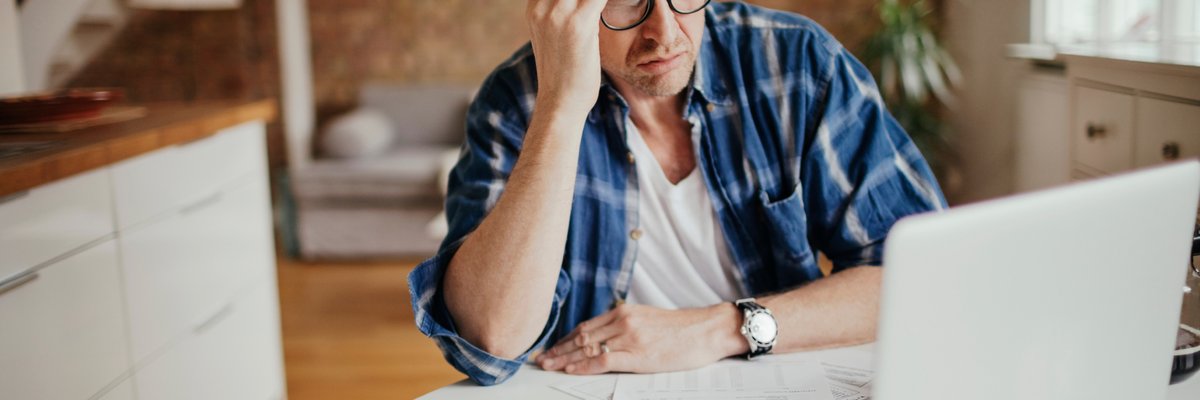 A person looks concerned at their financial documents and laptop.