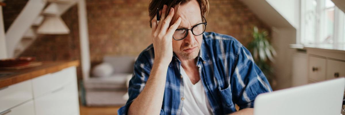 A person looks concerned at their financial documents and laptop.