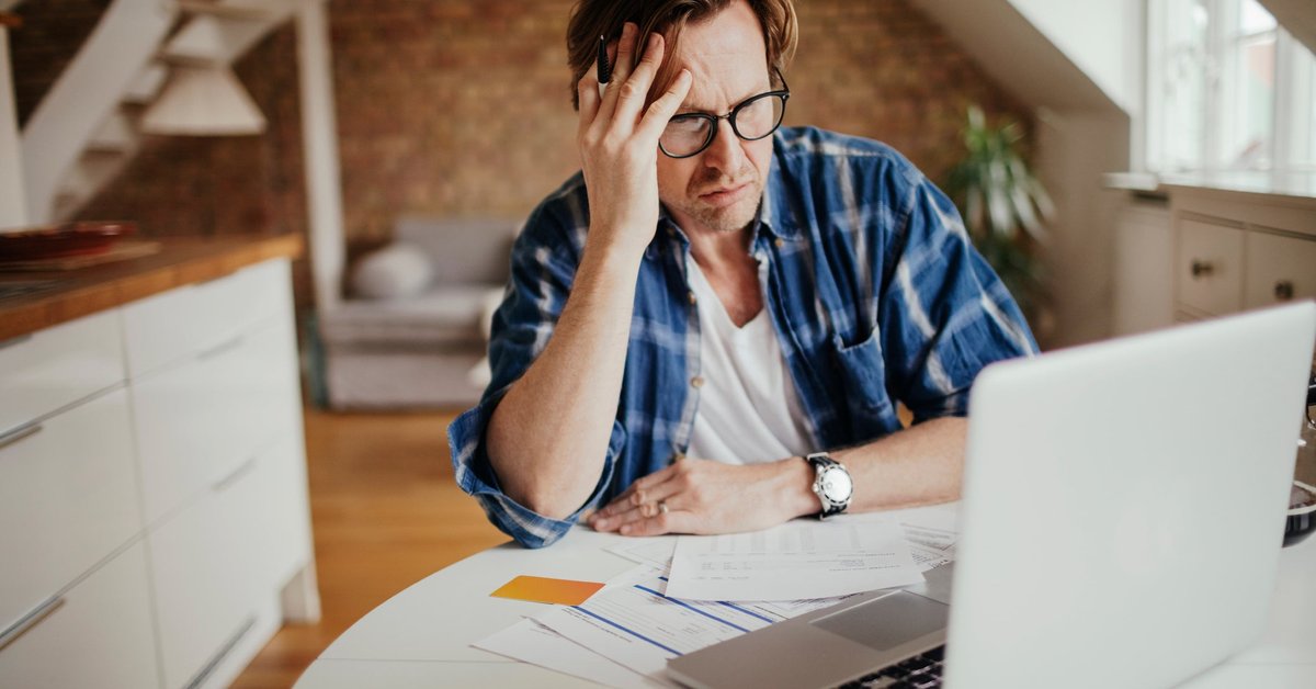 A person looks concerned at their financial documents and laptop.