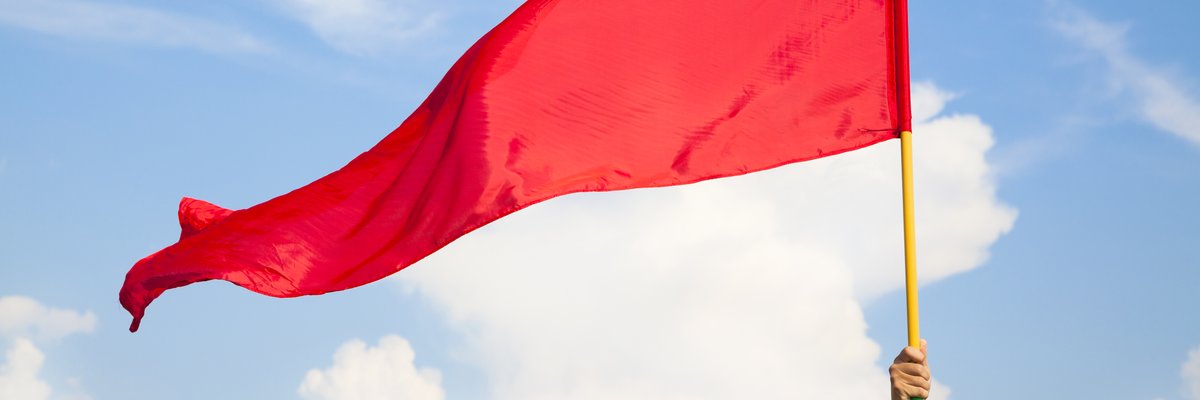 An arm raising a red flag with a background of blue sky and clouds.