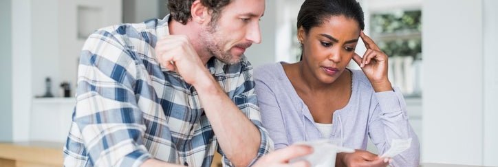 A couple looks at paperwork worriedly inside.