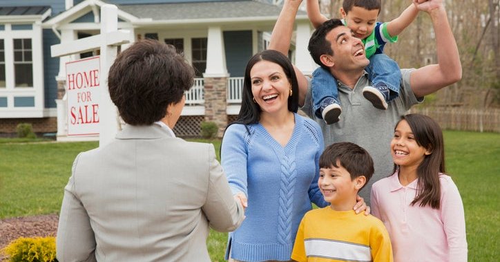 A parent shakes hands with a realtor as their family celebrates. A house with a sign that reads "Home for Sale" is behind them.