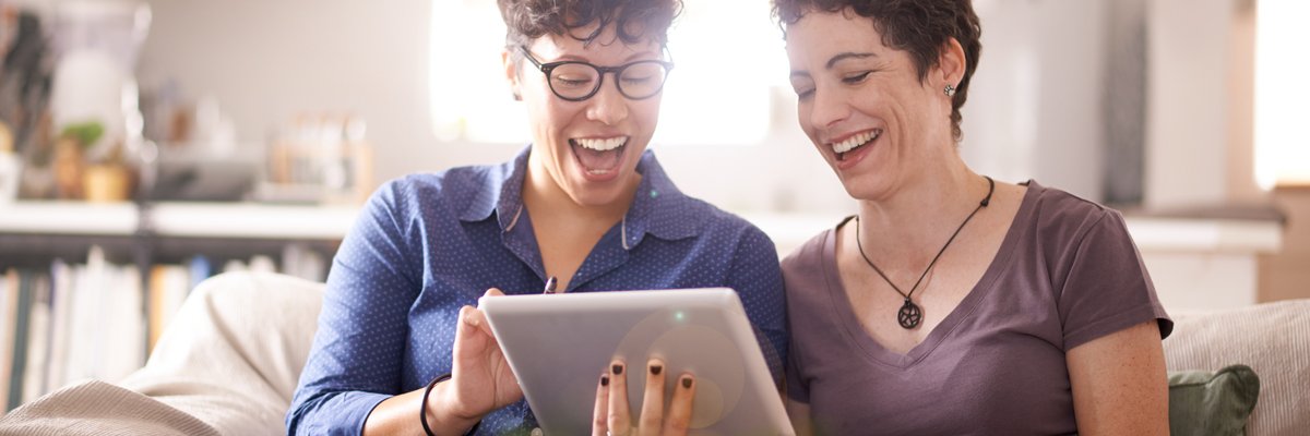 A couple smiles excitedly at their laptop screen in their living room.