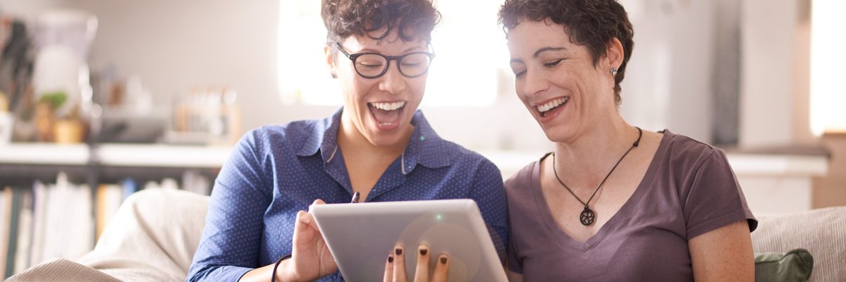 A couple smiles excitedly at their laptop screen in their living room.