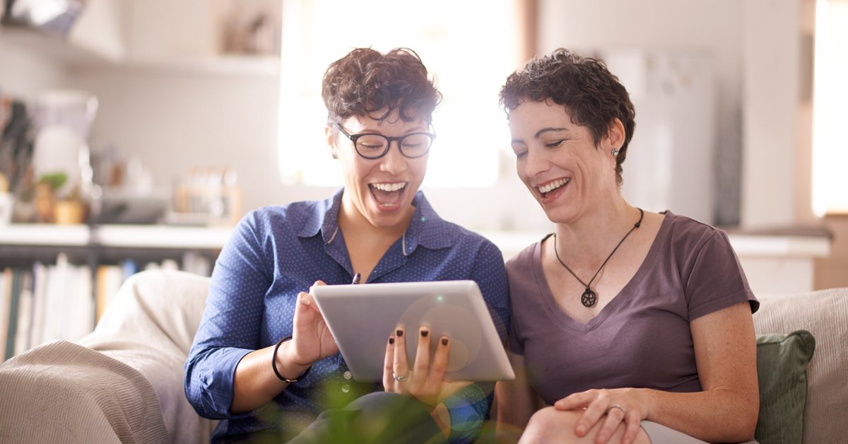 A couple smiles excitedly at their laptop screen in their living room.