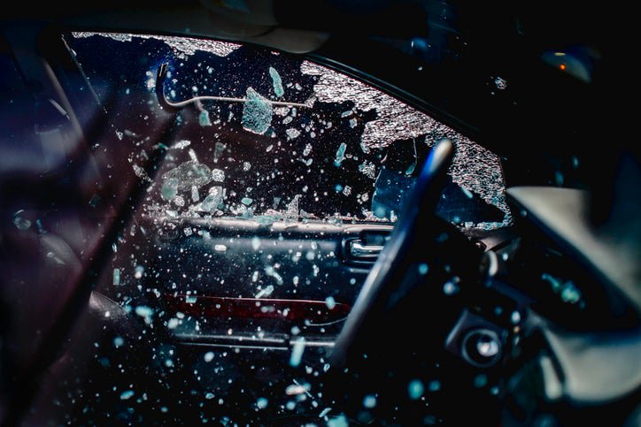 Car thief uses a crowbar to break into car. Many jagged pieces of glass in the air.