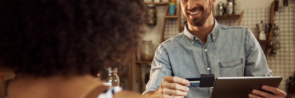 Barista grinning at customer as he swipes her card through an iPad reader.