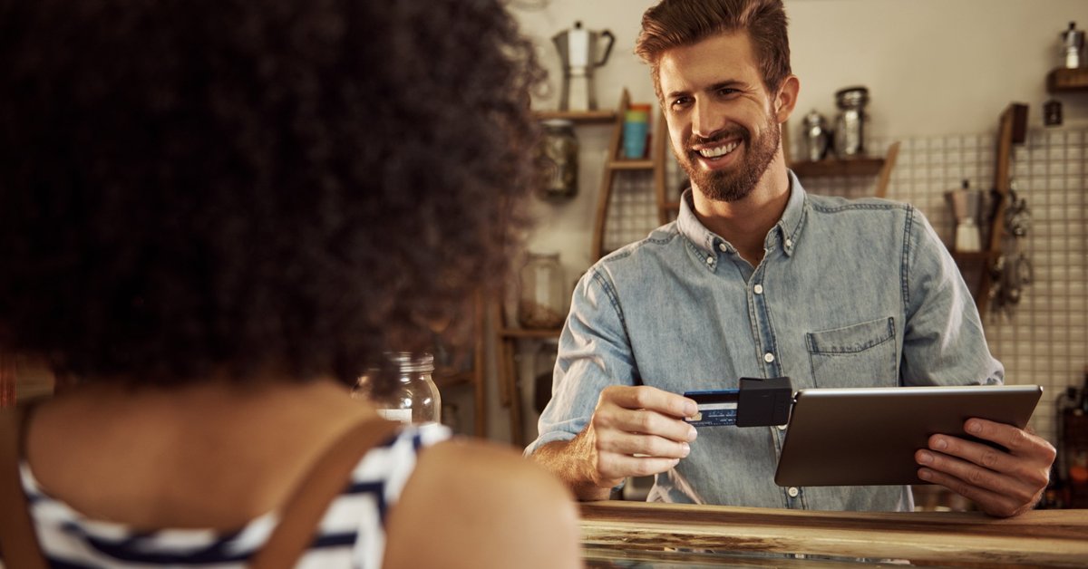 Barista grinning at customer as he swipes her card through an iPad reader.